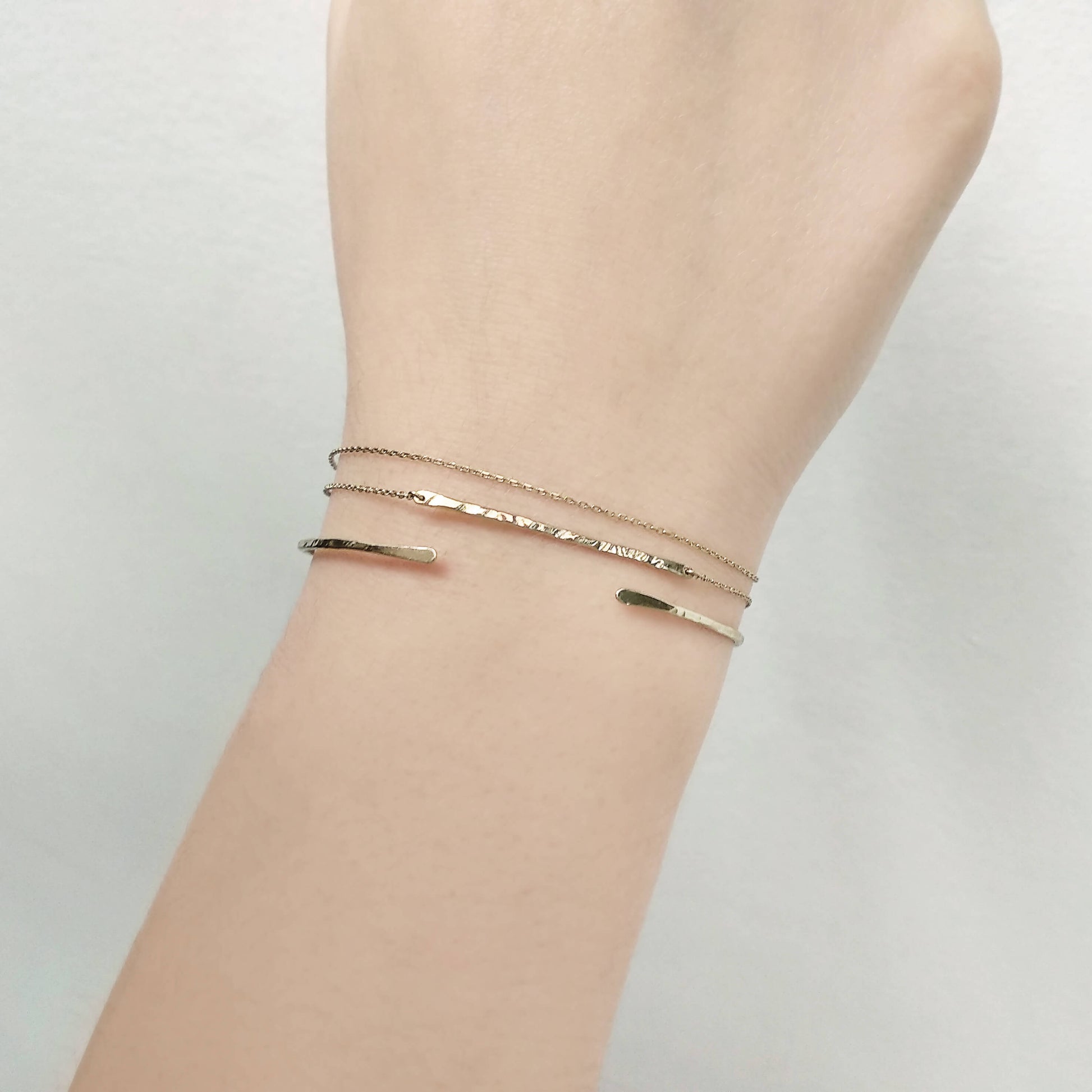 Two gold bracelets on a wrist against a plain background