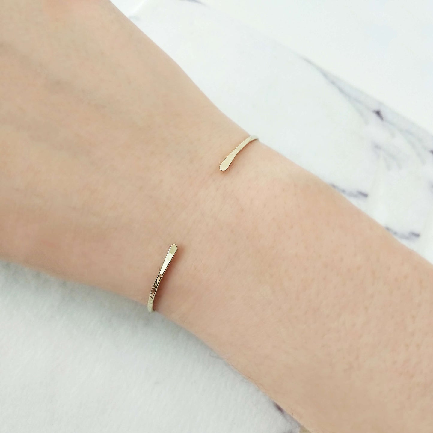 Gold cuff bracelet with hammered finish on a person's wrist with a marble background