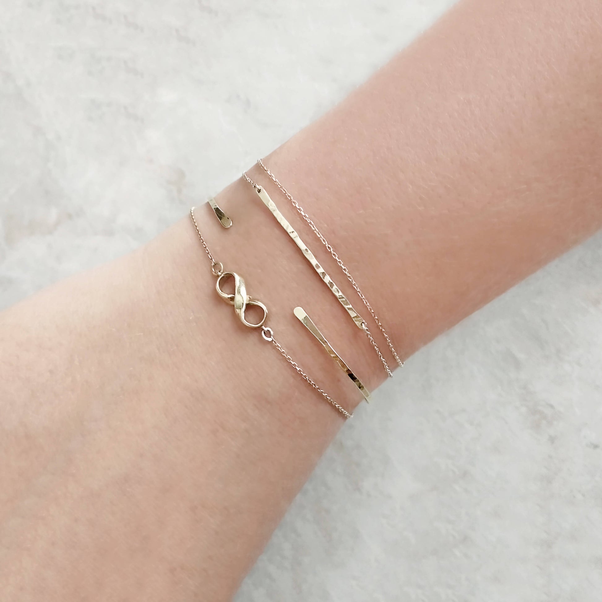Three gold bracelets on a wrist against a light background