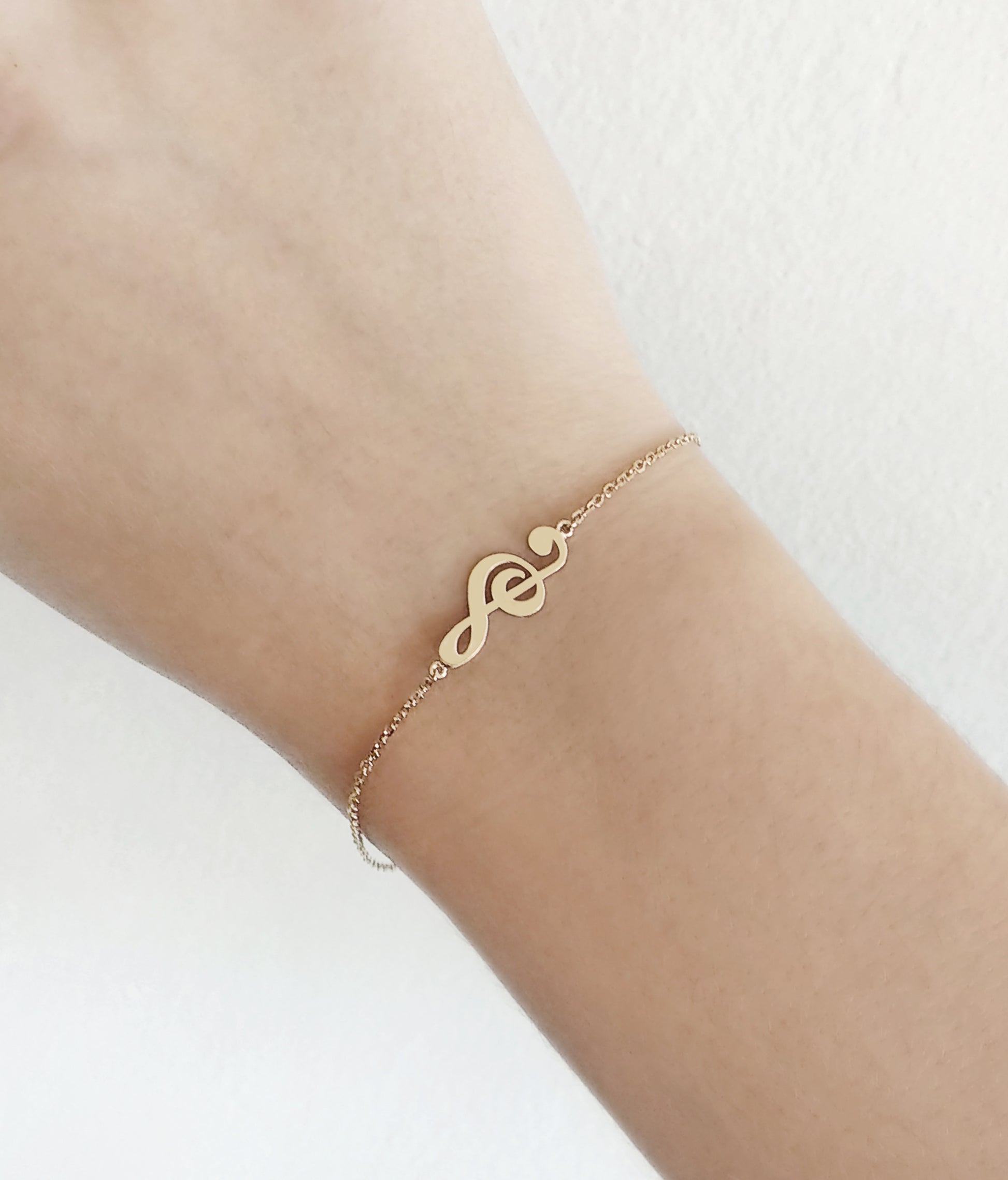 woman's wrist wearing gold treble clef music charm bracelet