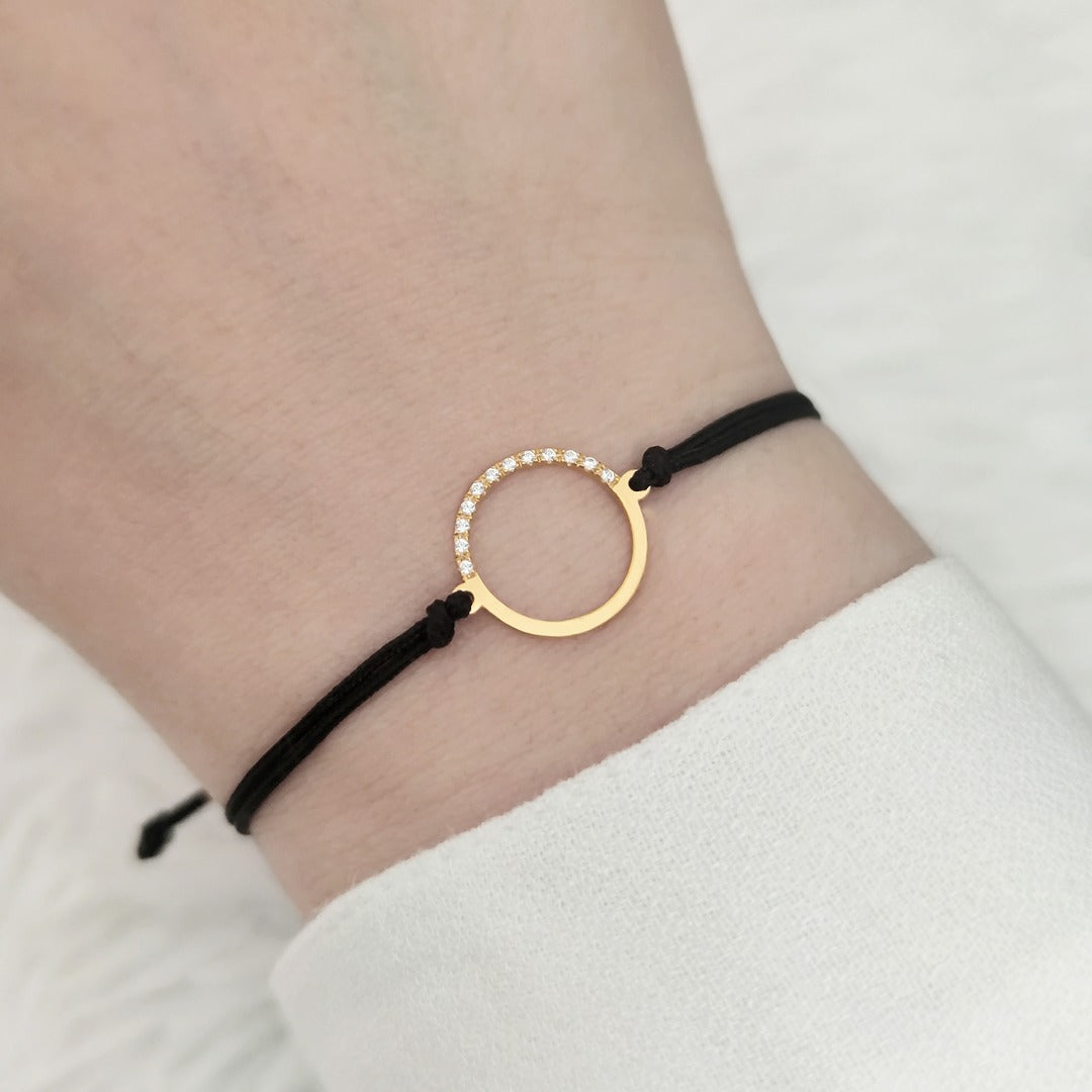 female wrist wearing solid yellow gold macrame bracelet with a circle charm set with 12 white diamonds on its two corners