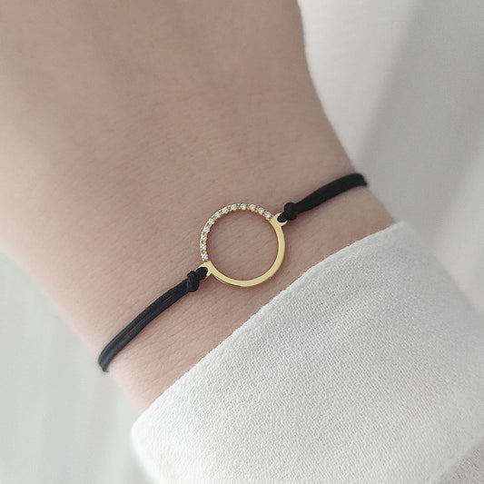 female wrist wearing solid yellow gold macrame bracelet with a circle charm set with 12 white diamonds on its two corners