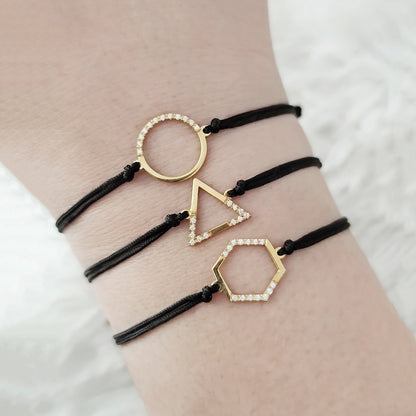 female wrist wearing three solid gold macrame bracelets with geometric charms, circle, triangle and hexagon set with diamonds