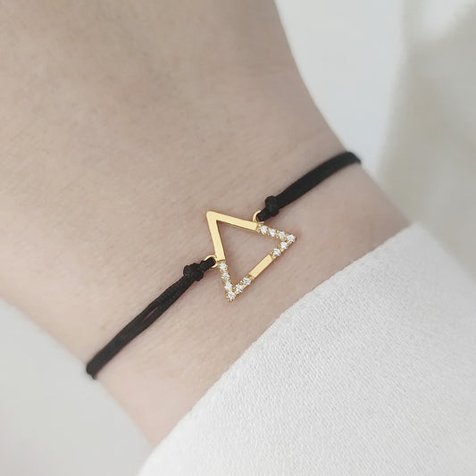 woman's wrist wearing solid yellow gold macrame bracelet with a small triangle charm set with 12 white diamonds on its two corners