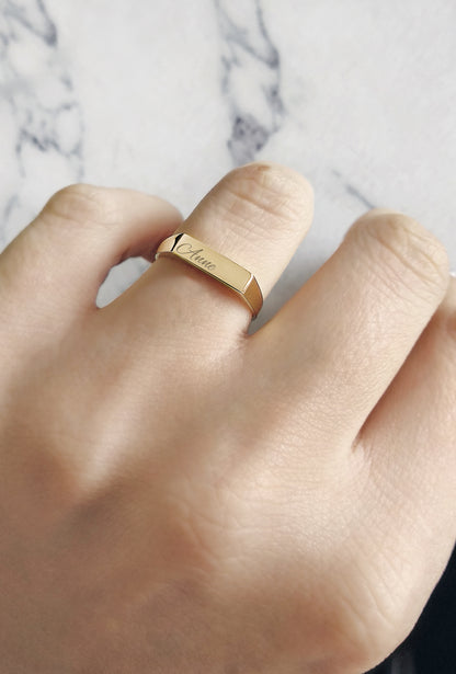 woman's hand wearing solid yellow gold rectangle bar signet ring on her ring finger personalized with engraving