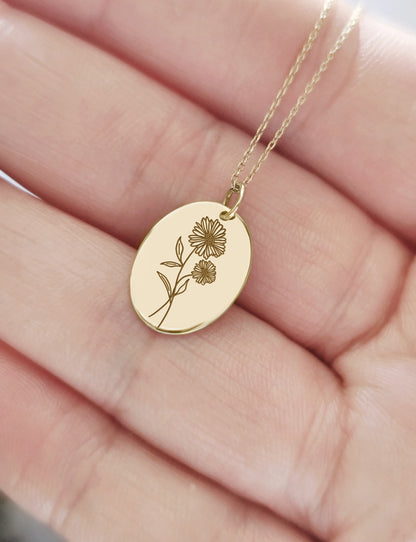 hand holding yellow gold oval pendant necklace engraved with the birth flower of April Daisy for size reference