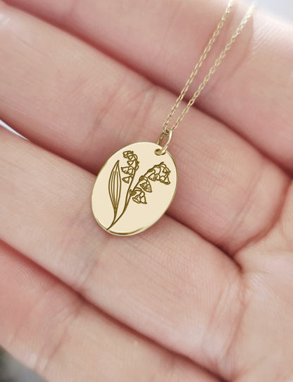 hand holding gold oval pendant necklace engraved with Lily of the Valley birth flower of May for size reference