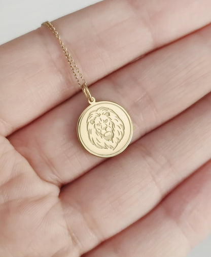 hand holding for size reference a yellow gold disc pendant necklace engraved with a lion head and a circle frame around it