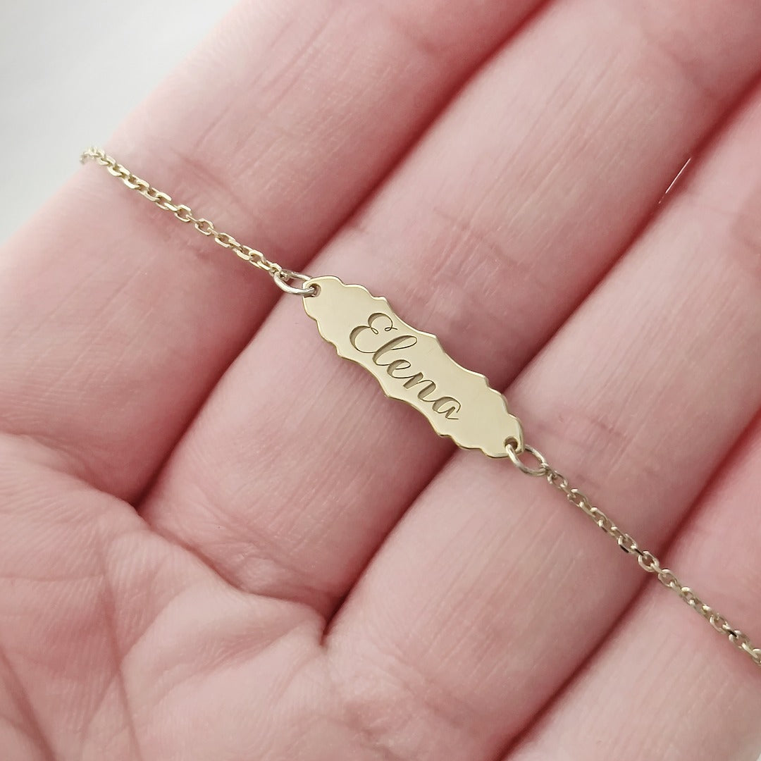 hand holding a gold bracelet with a vintage baroque inspired bar engraved with a name