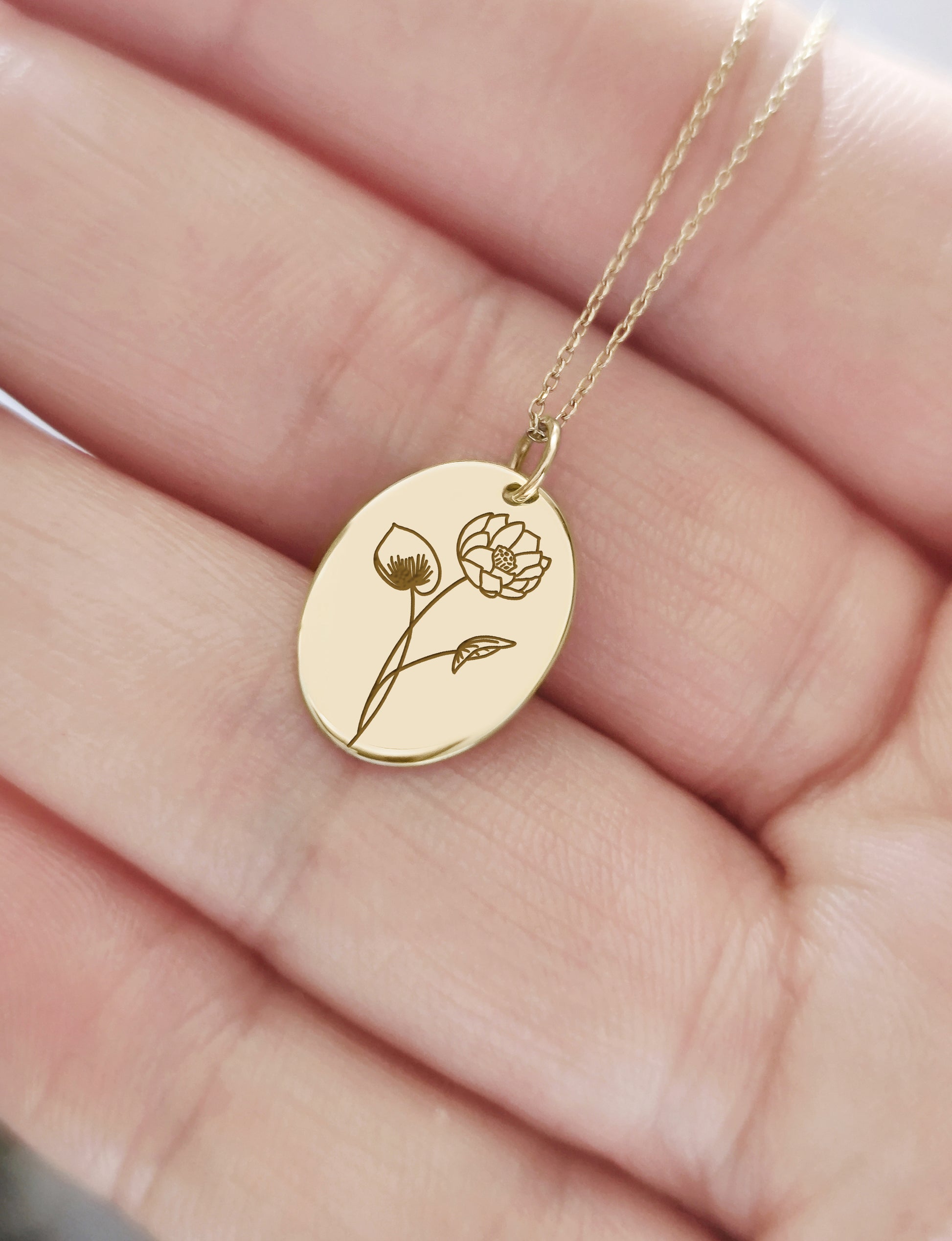 female had holding a solid gold oval pendant necklace engraved with a Water Lily the birth flower of July 