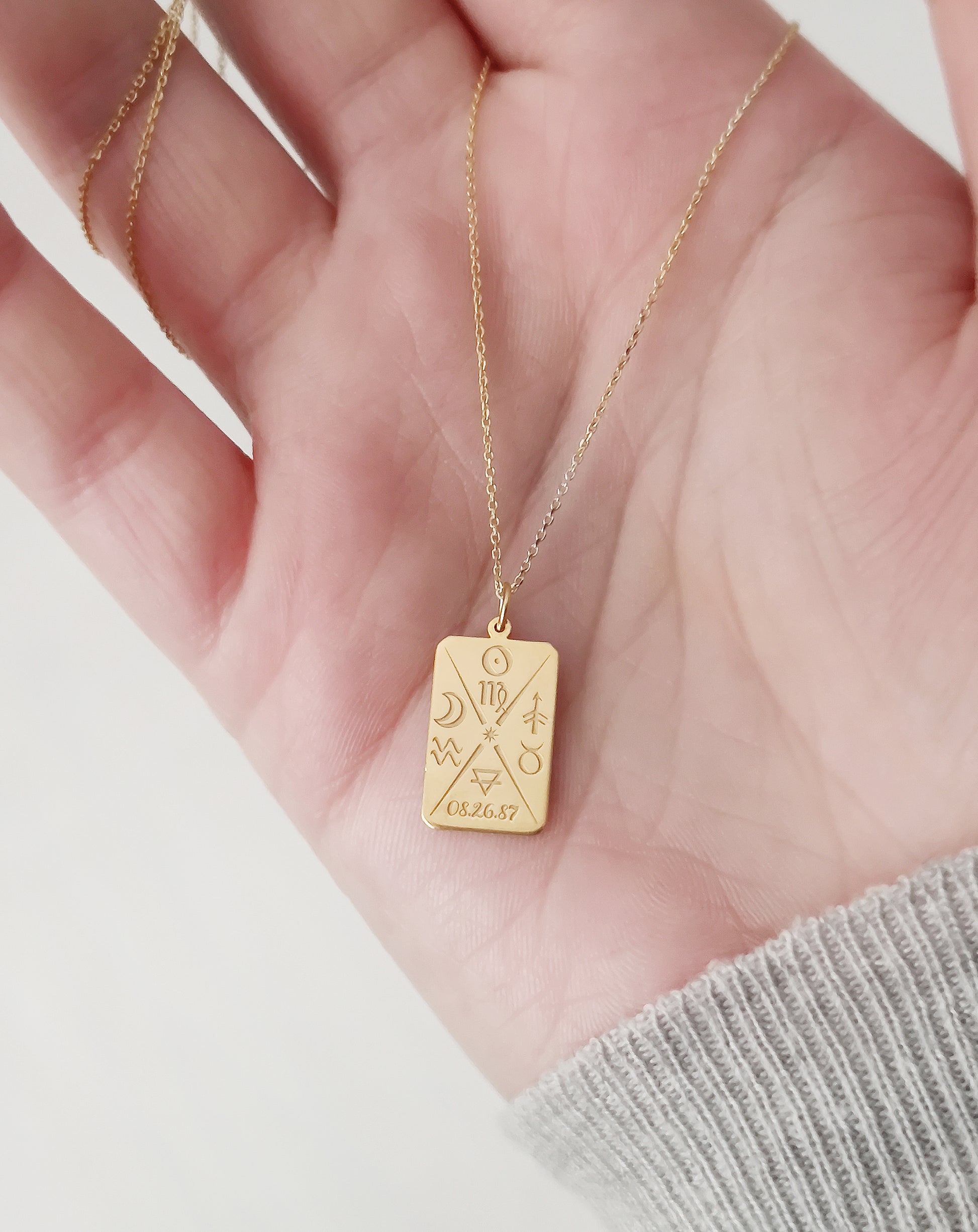 hand holding gold octagon pendant necklace personalized with natal chart zodiac signs of the sun the moon and ascendant, a birth date and an alchemy element