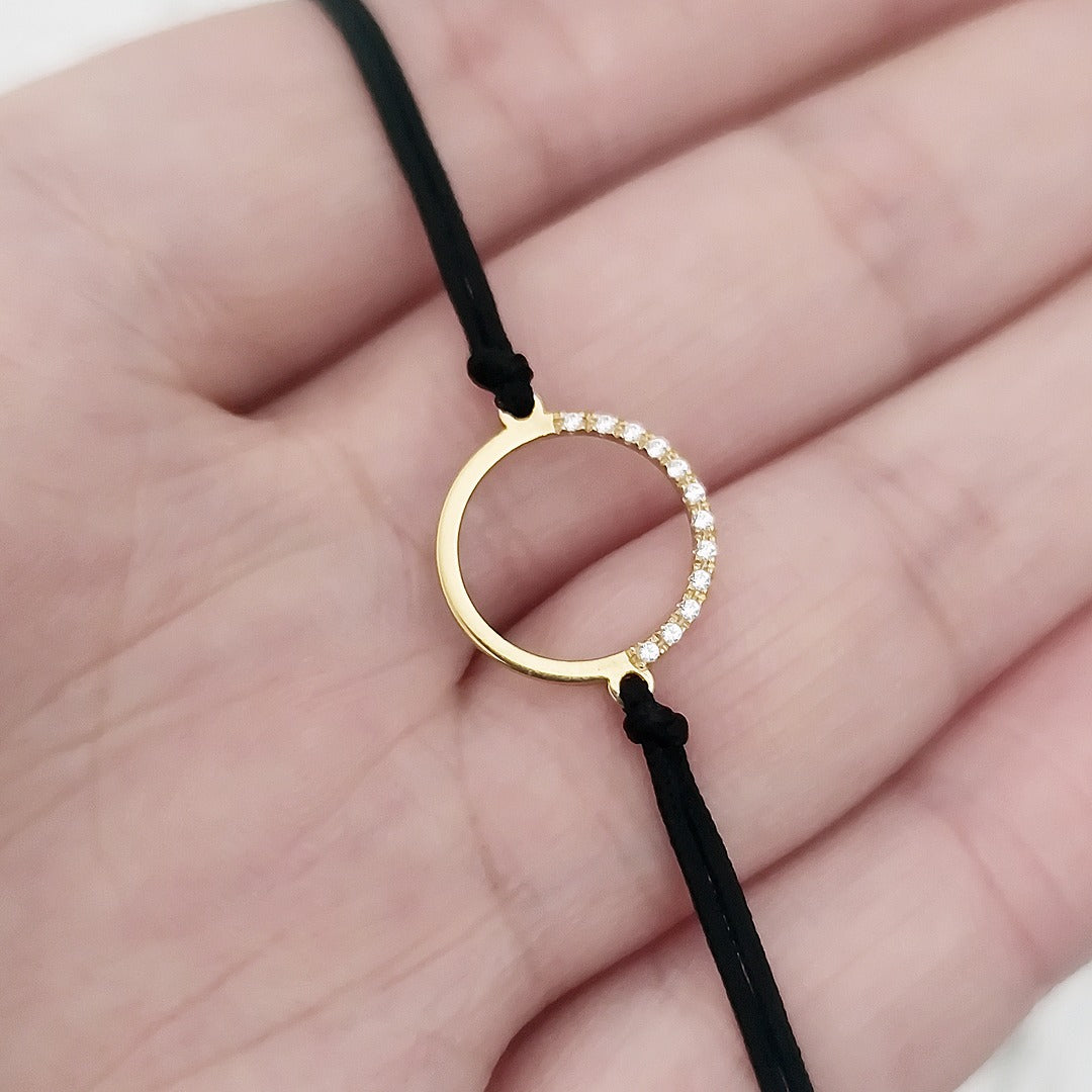 hand holding a solid yellow gold macrame bracelet with a circle charm set with 12 white diamonds on its two corners