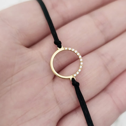 hand holding a solid yellow gold macrame bracelet with a circle charm set with 12 white diamonds on its two corners