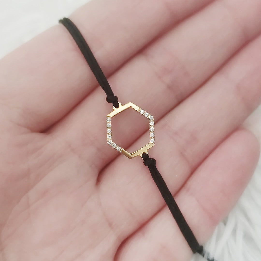 Gold hexagonal charm bracelet with diamonds and black cord on a hand