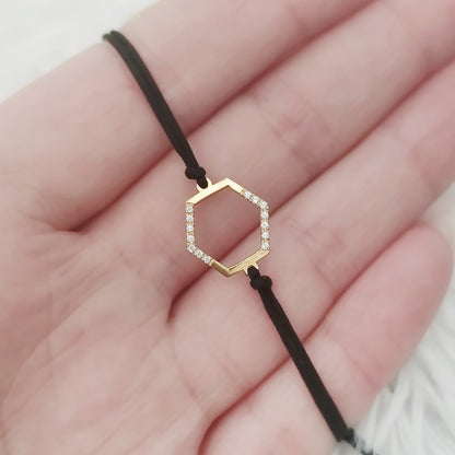 Gold hexagonal charm bracelet with diamonds and black cord on a hand