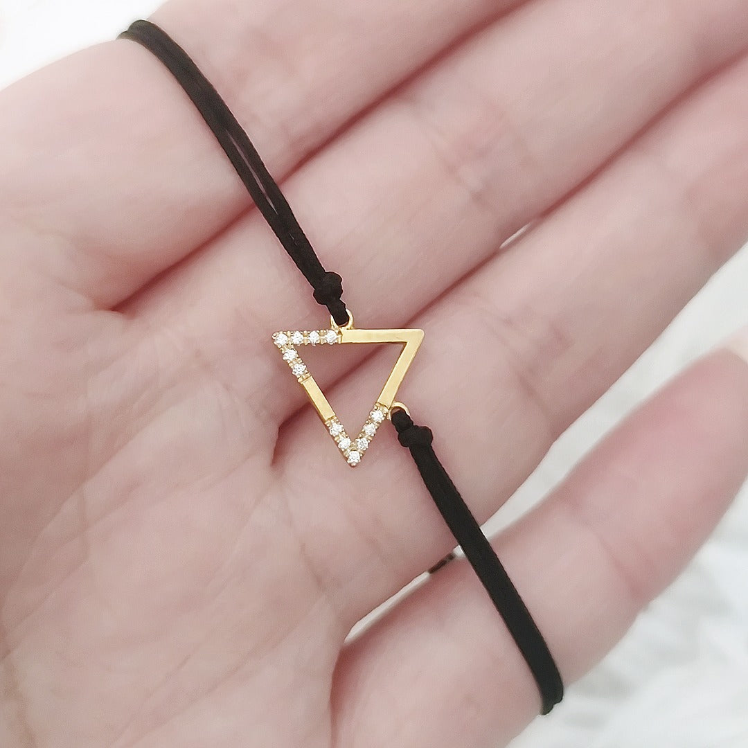 hand holding a yellow gold macrame bracelet with a small triangle charm set with 12 white diamonds on its two corners