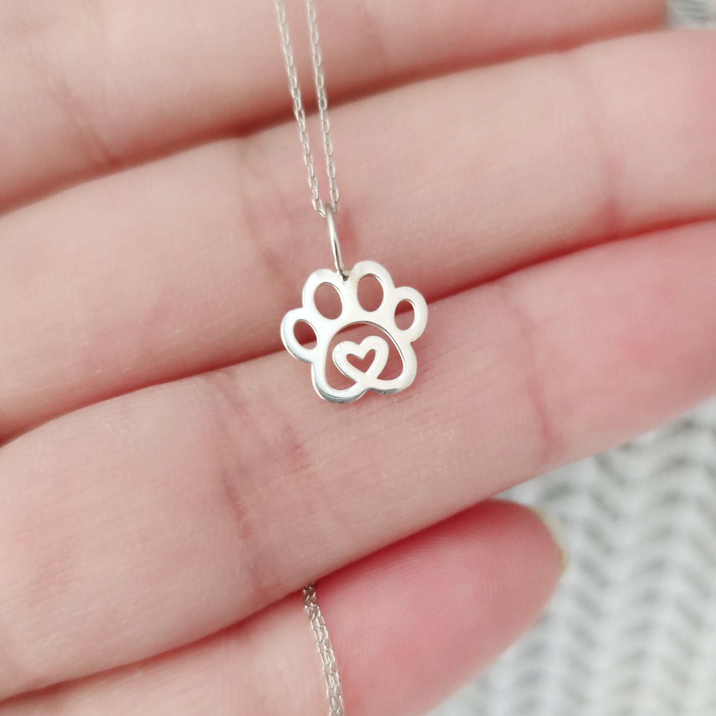 hand holding solid gold necklace with a tiny dog paw print pendant with a heart in the center