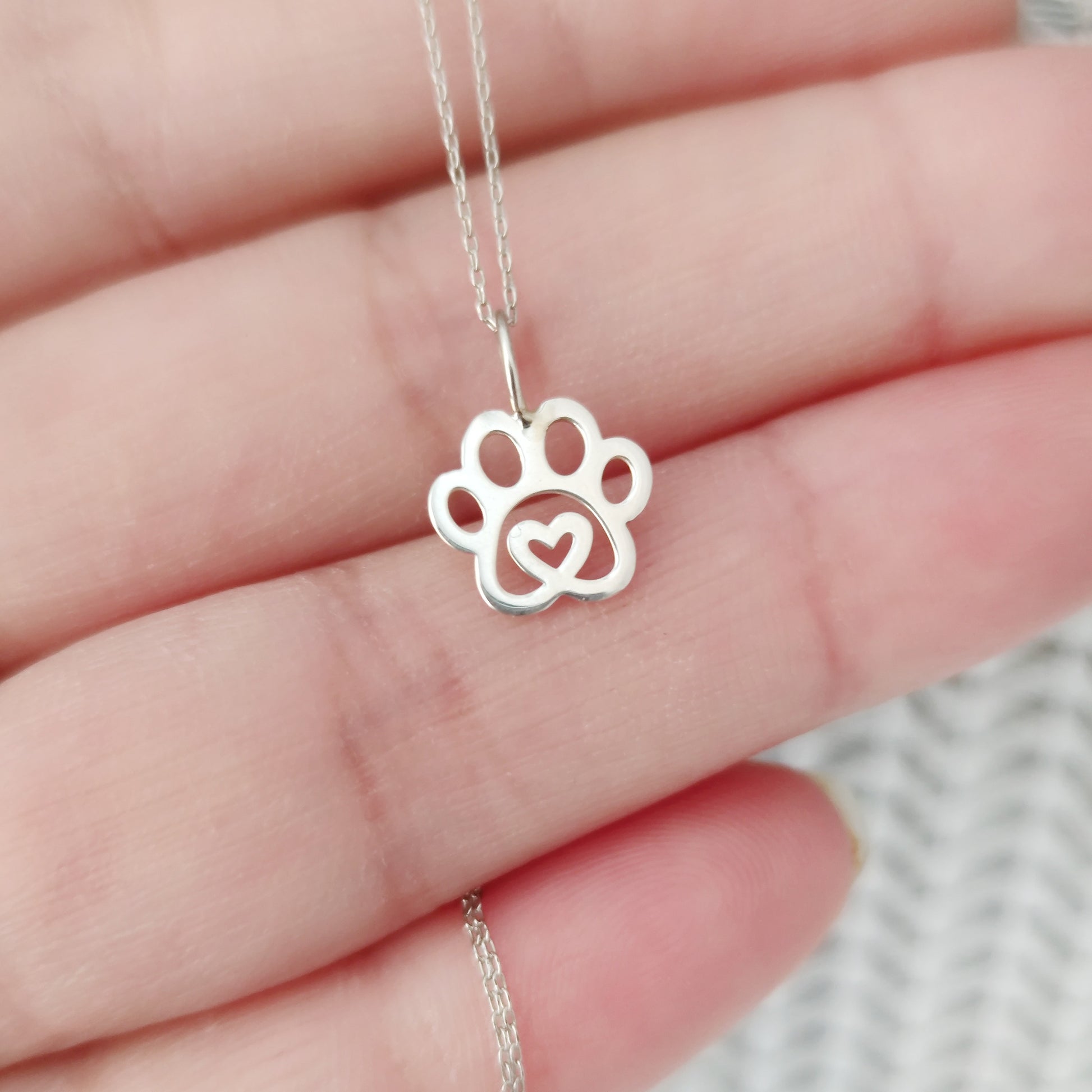 hand holding solid gold necklace with a tiny dog paw print pendant with a heart in the center
