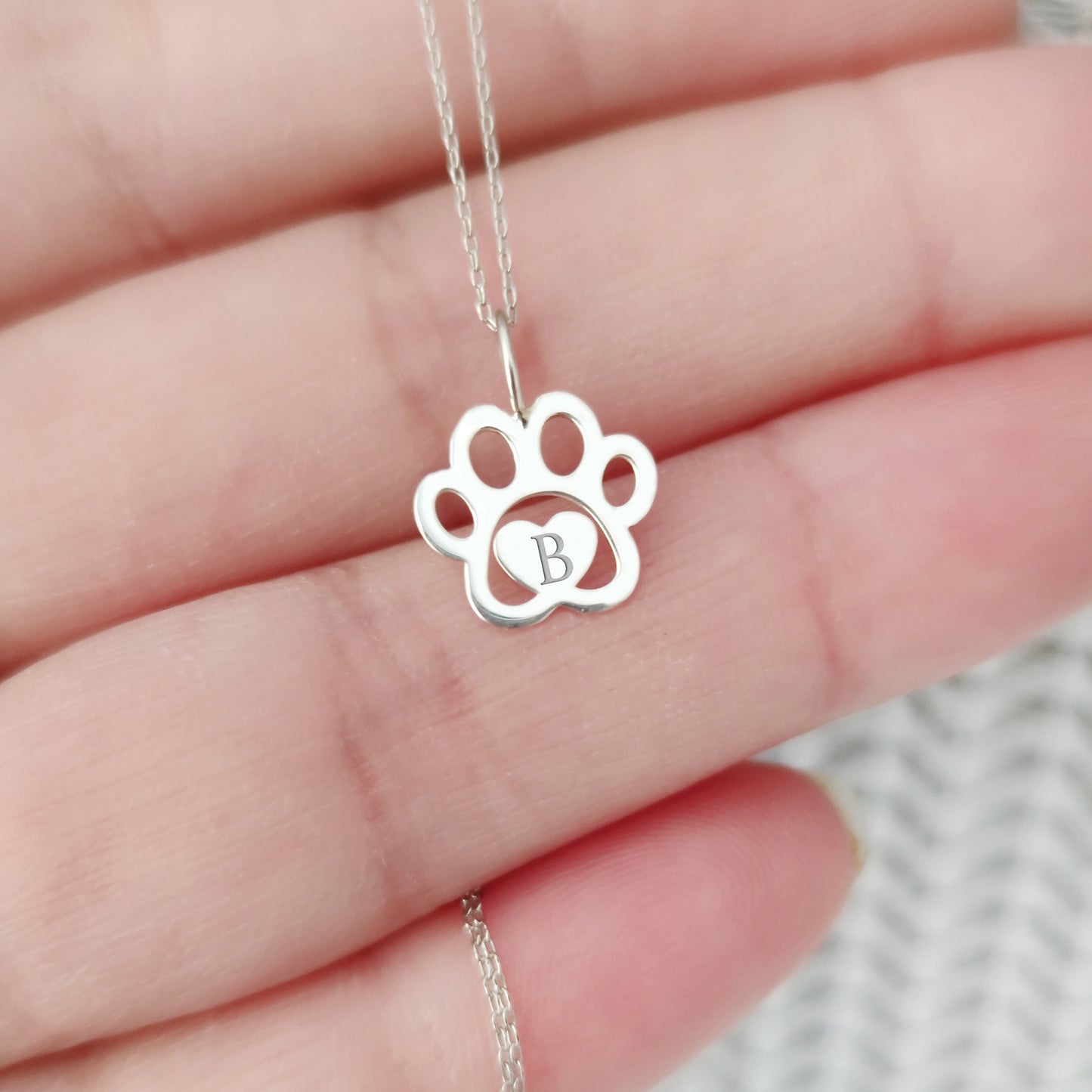 hand holding a white gold necklace with a dog paw print pendant engraved with a monogram