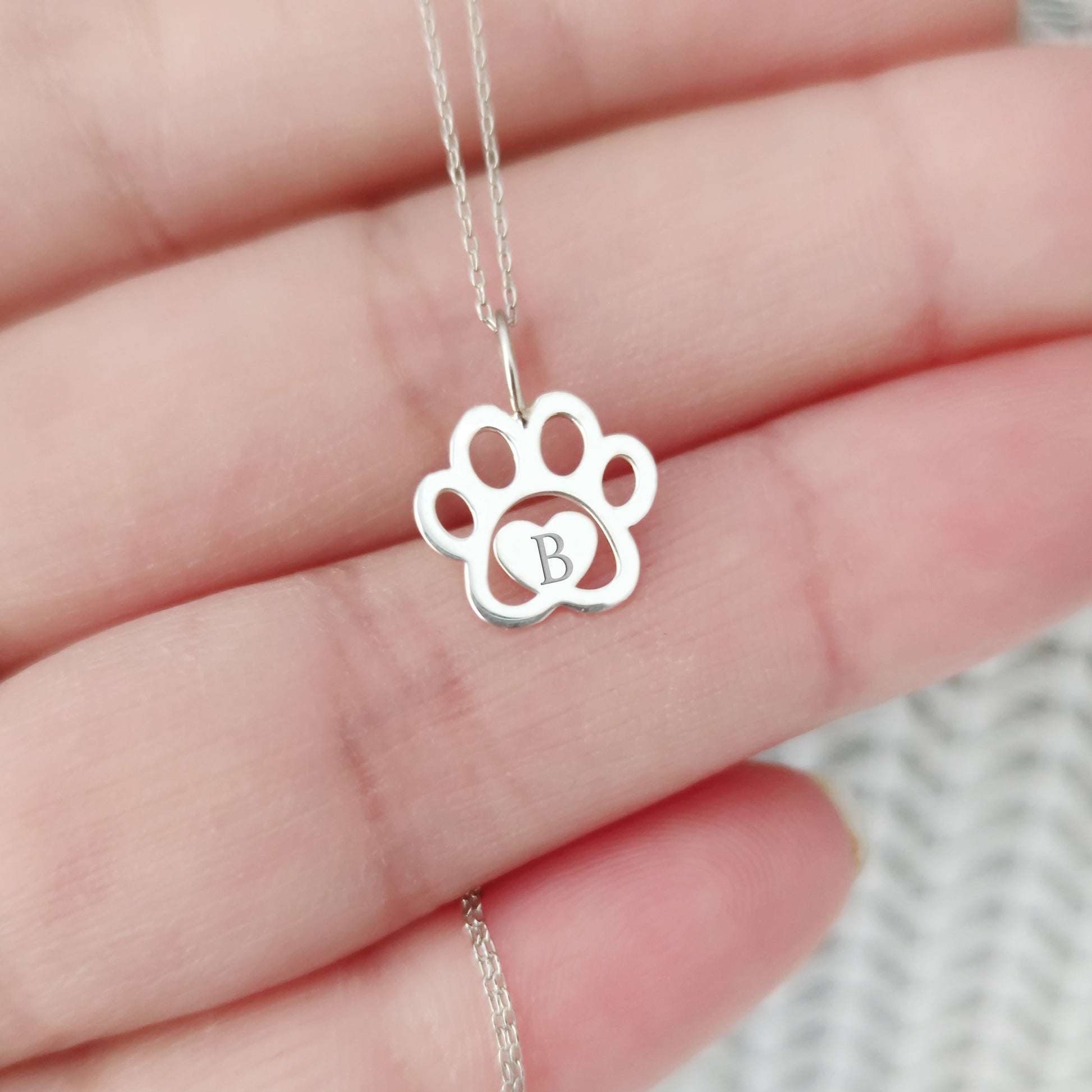 hand holding a white gold necklace with a dog paw print pendant engraved with a monogram