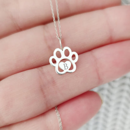 hand holding a white gold necklace with a dog paw print pendant engraved with a monogram