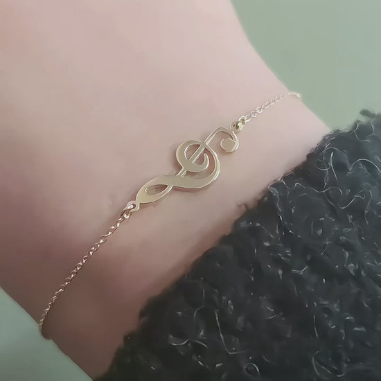 video of a woman's wrist wearing a solid yellow gold treble clef music charm bracelet