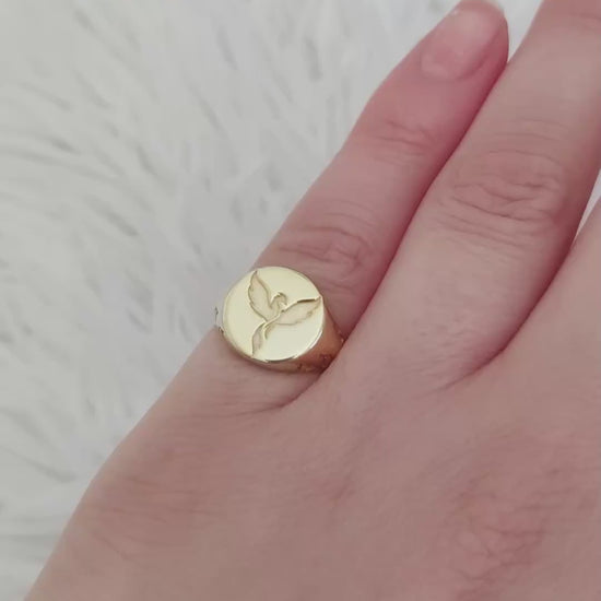 video of a woman's hand wearing a gold polished and a matte white gold round signet ring engraved with a phoenix firebird with flame cutouts around the base of the ring's head