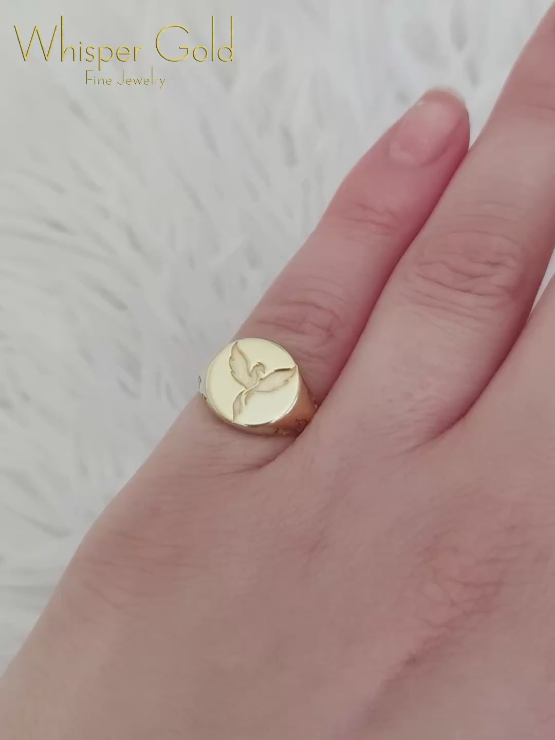 video of a woman's hand wearing a gold polished and a matte white gold round signet ring engraved with a phoenix firebird with flame cutouts around the base of the ring's head