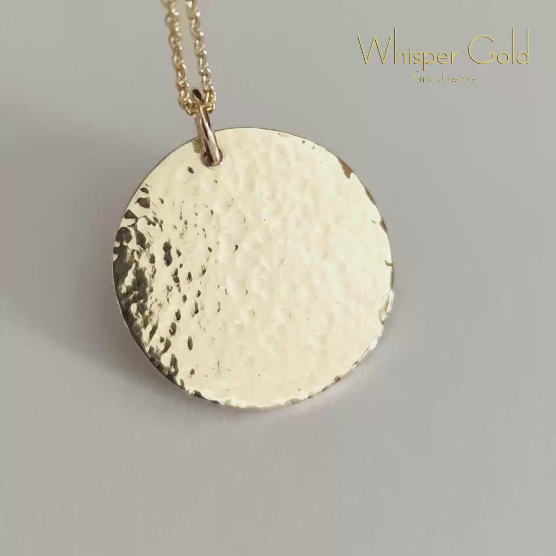 close-up video of a gold necklace with a round hammered pendant on a light gray background
