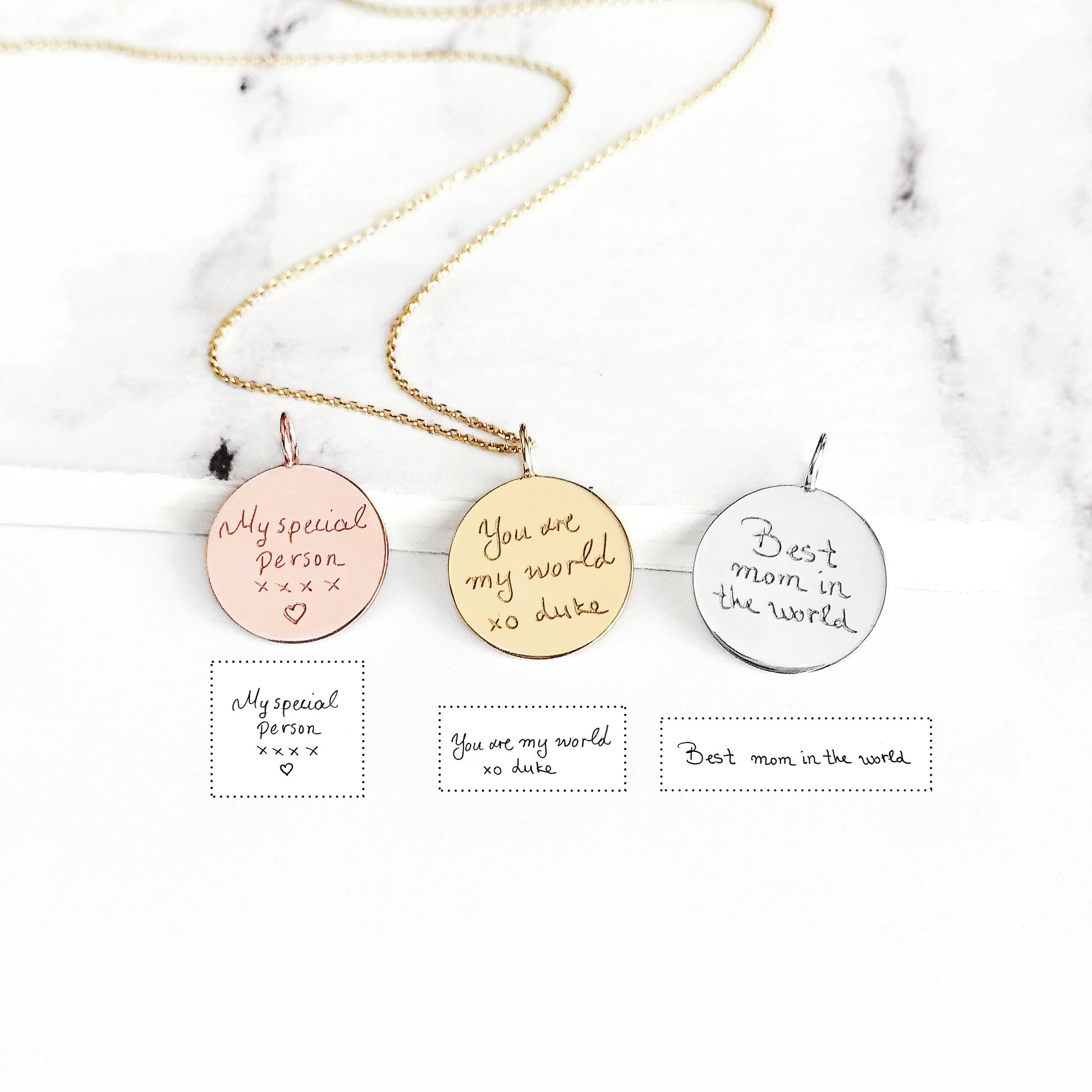 Three round pendants with personalized handwriting engravings on a marble background