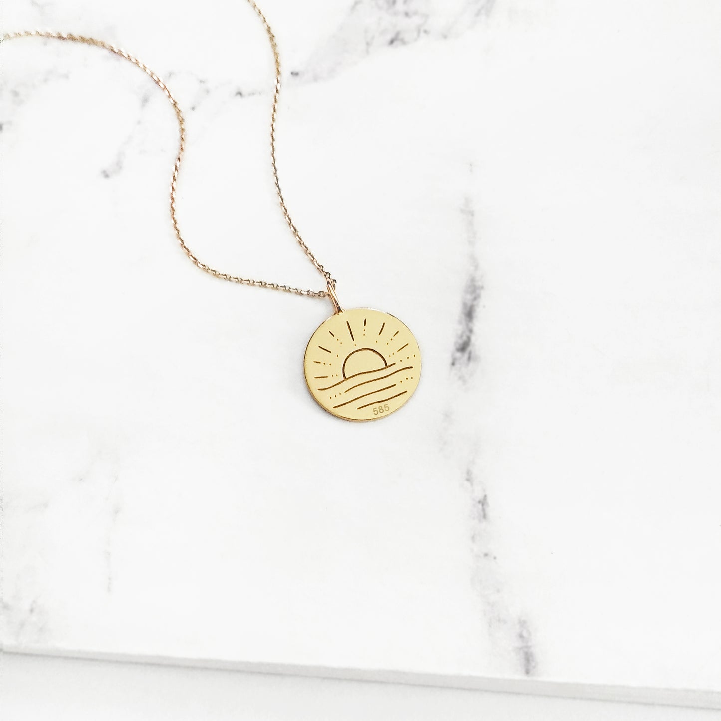 Gold necklace with a round pendant engraved with a sun on a marble surface