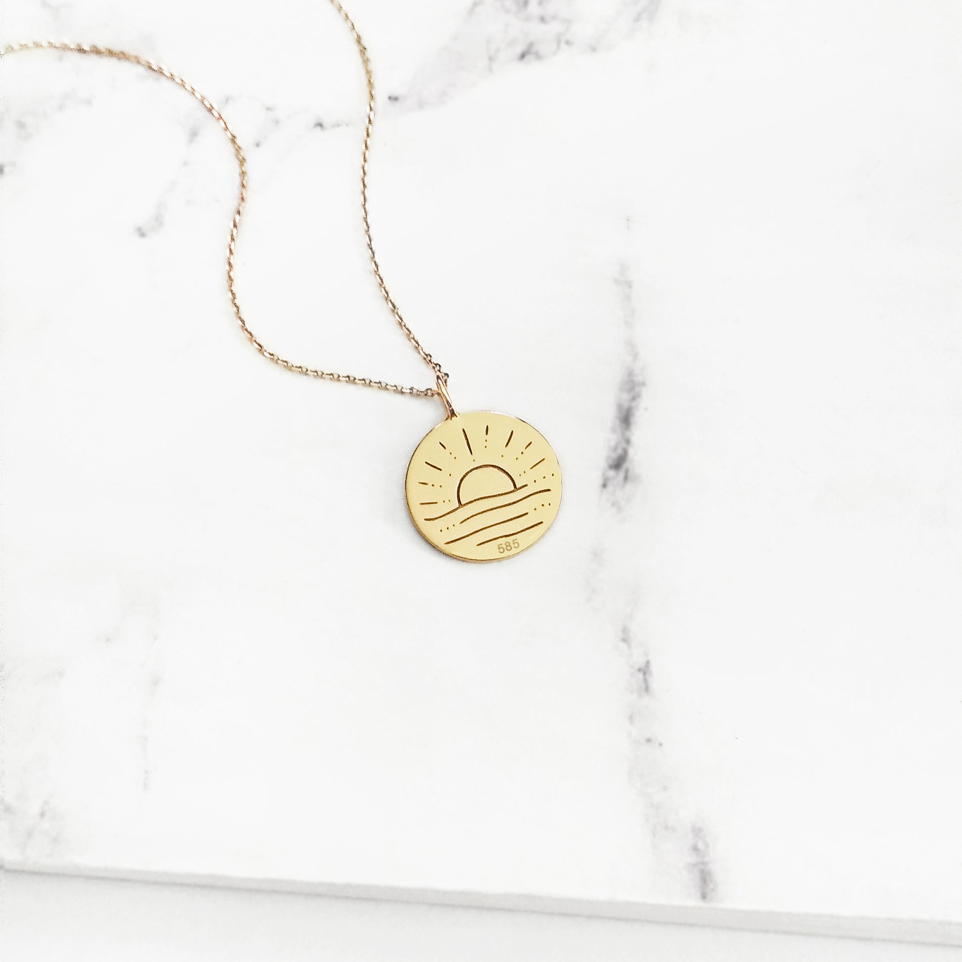 Gold necklace with a round pendant engraved with a sun on a marble surface