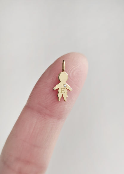 close up of a fingertip holding a tiny gold boy outline charm engraved with an initial and set with a tiny diamond for size reference
