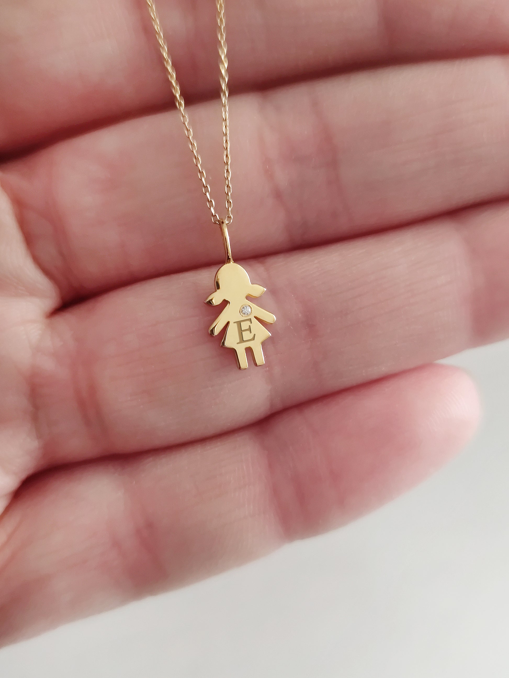 close up of a palm holding a gold necklace with a tiny girl outline charm set with a diamond and engraved with an initial for size reference