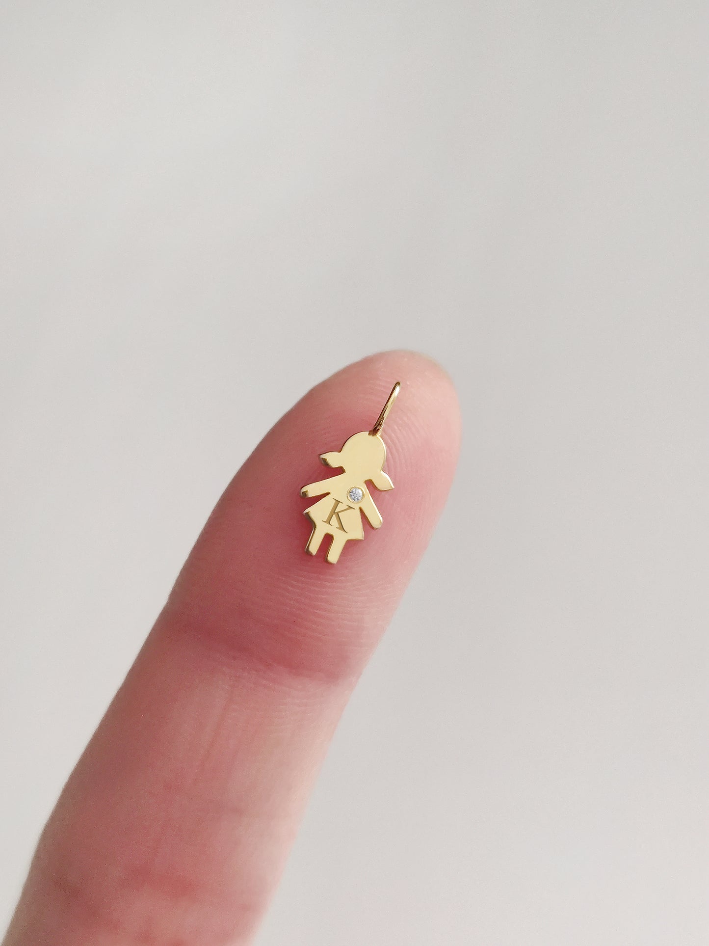 close up of a fingertip holding a tiny gold girl outline charm engraved with an initial and set with a tiny diamond for size reference