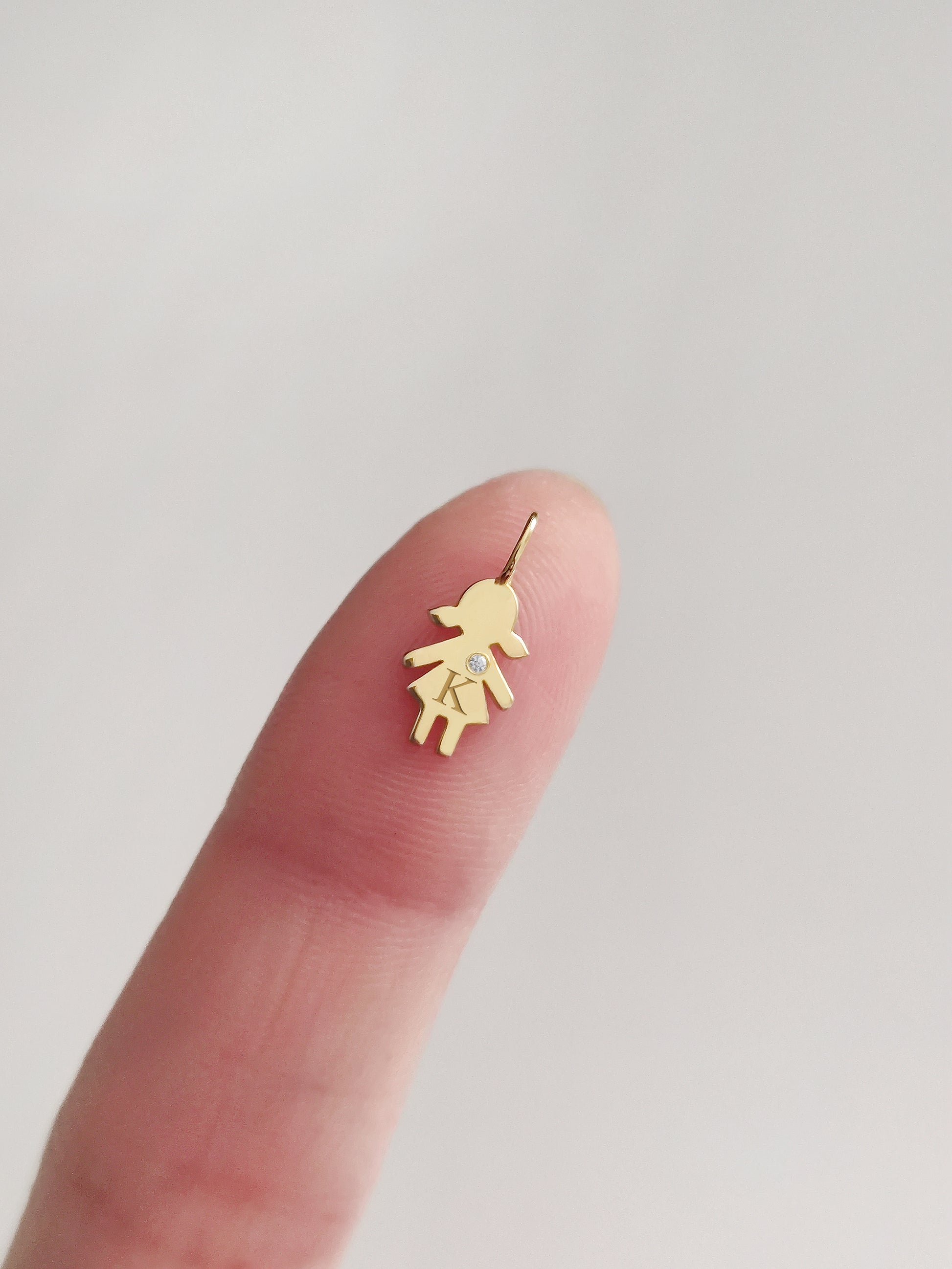 close up of a fingertip holding a tiny gold girl outline charm engraved with an initial and set with a tiny diamond for size reference