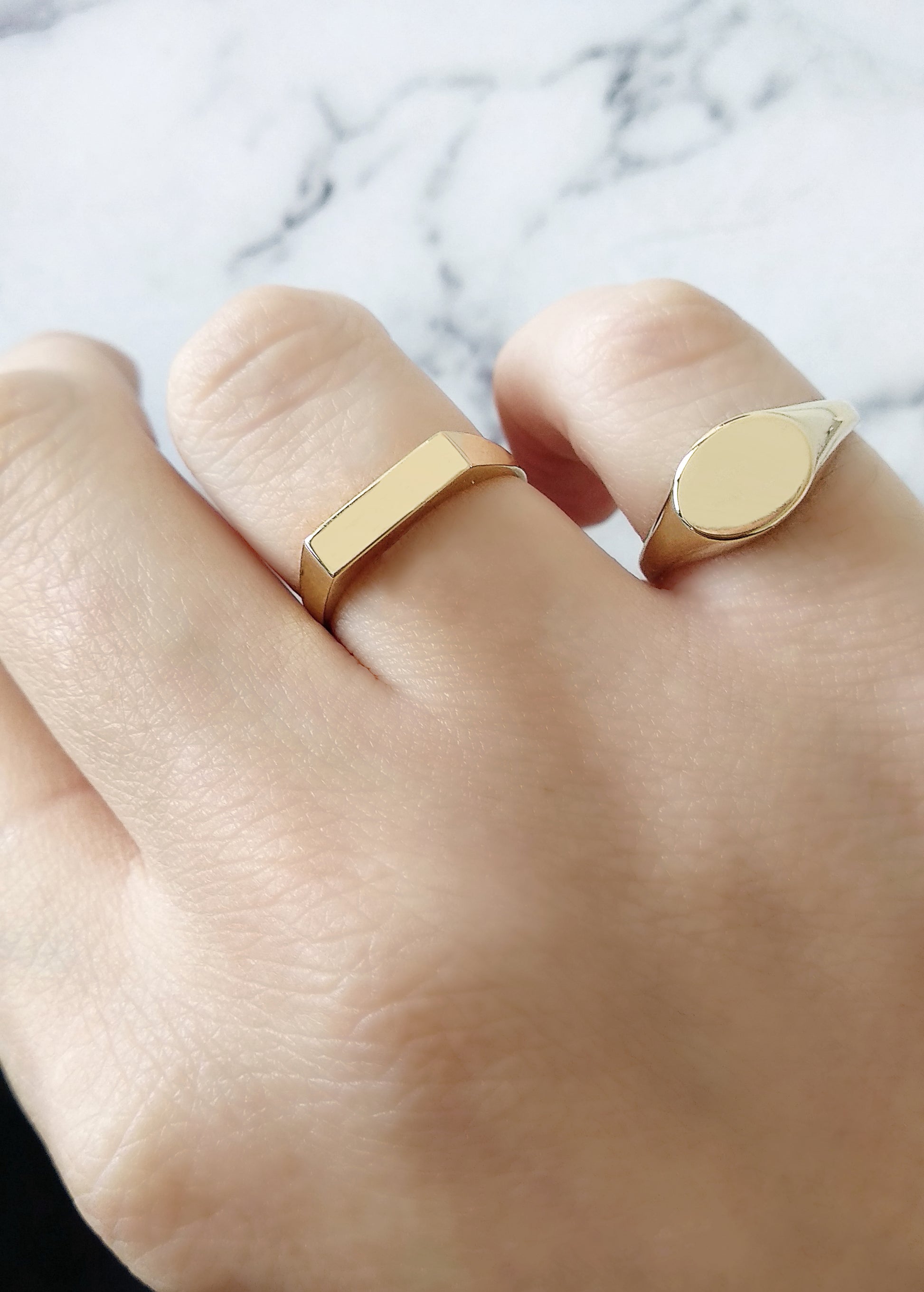 female hand wearing solid yellow gold rectangle bar signet ring on the ring finger and an oval signet ring on her pinky