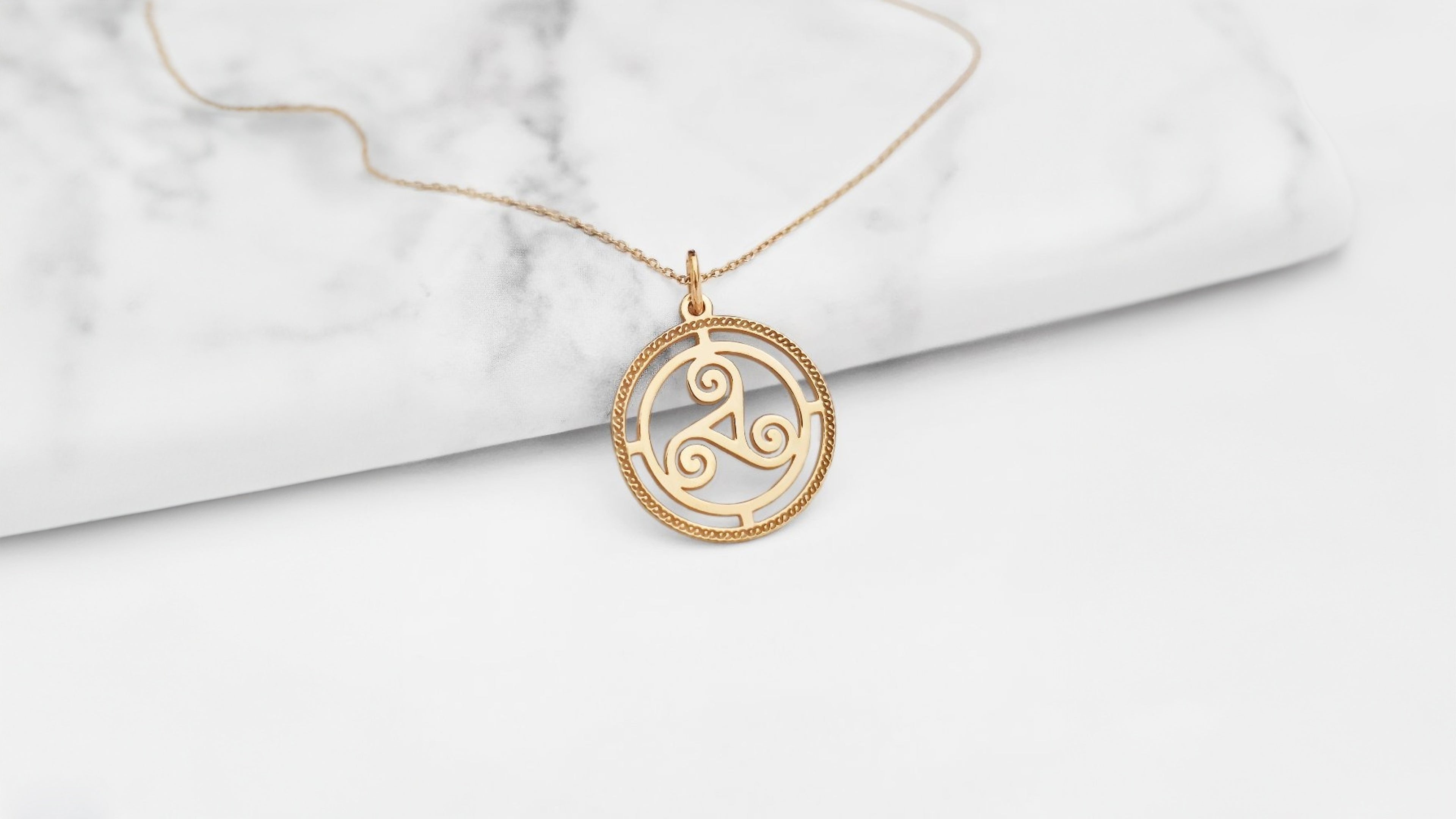 Gold necklace with a circular triskelion pendant on a marble surface