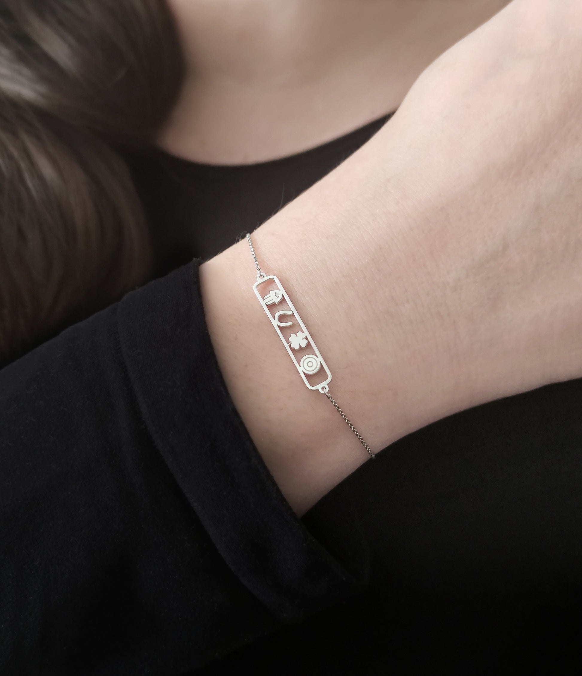 woman wearing an open bar bracelet with four lucky charms, a hamsa, a horseshoe, a clover and an evil eye made in solid gold
