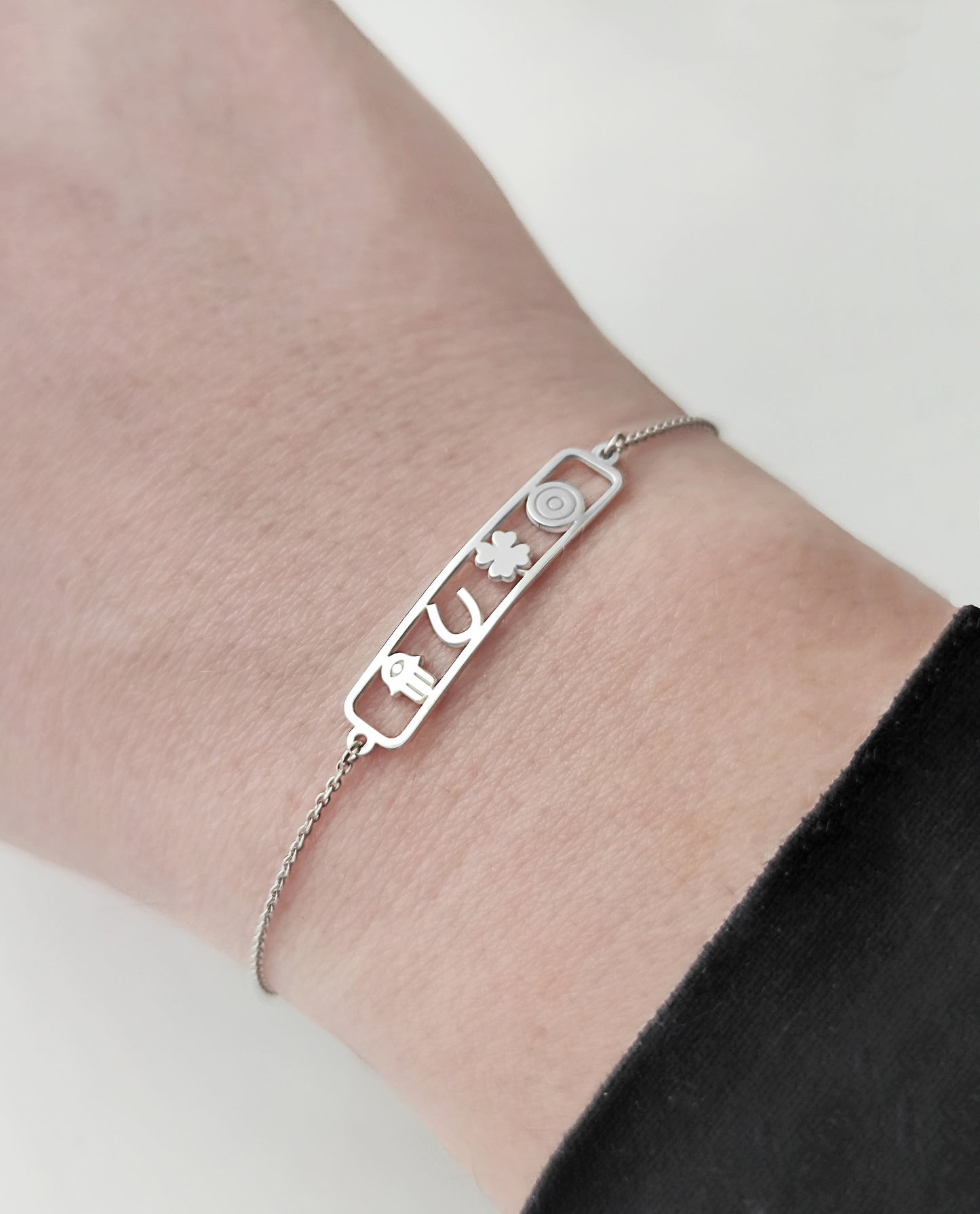 woman's wrist wearing an open bar bracelet with four lucky charms, a hamsa, a horseshoe, a clover and an evil eye made in solid gold