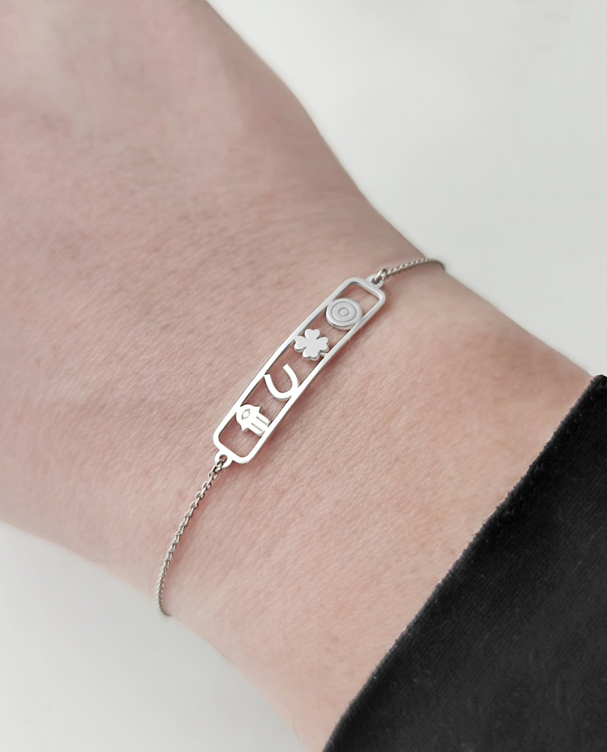 woman's wrist wearing an open bar bracelet with four lucky charms, a hamsa, a horseshoe, a clover and an evil eye made in solid gold
