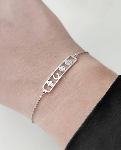 woman's wrist wearing an open bar bracelet with four lucky charms, a hamsa, a horseshoe, a clover and an evil eye made in solid gold