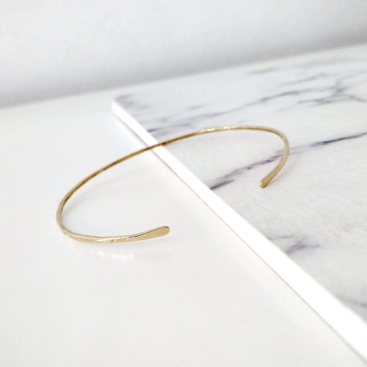 Thin gold hammered open bangle bracelet on a marble surface