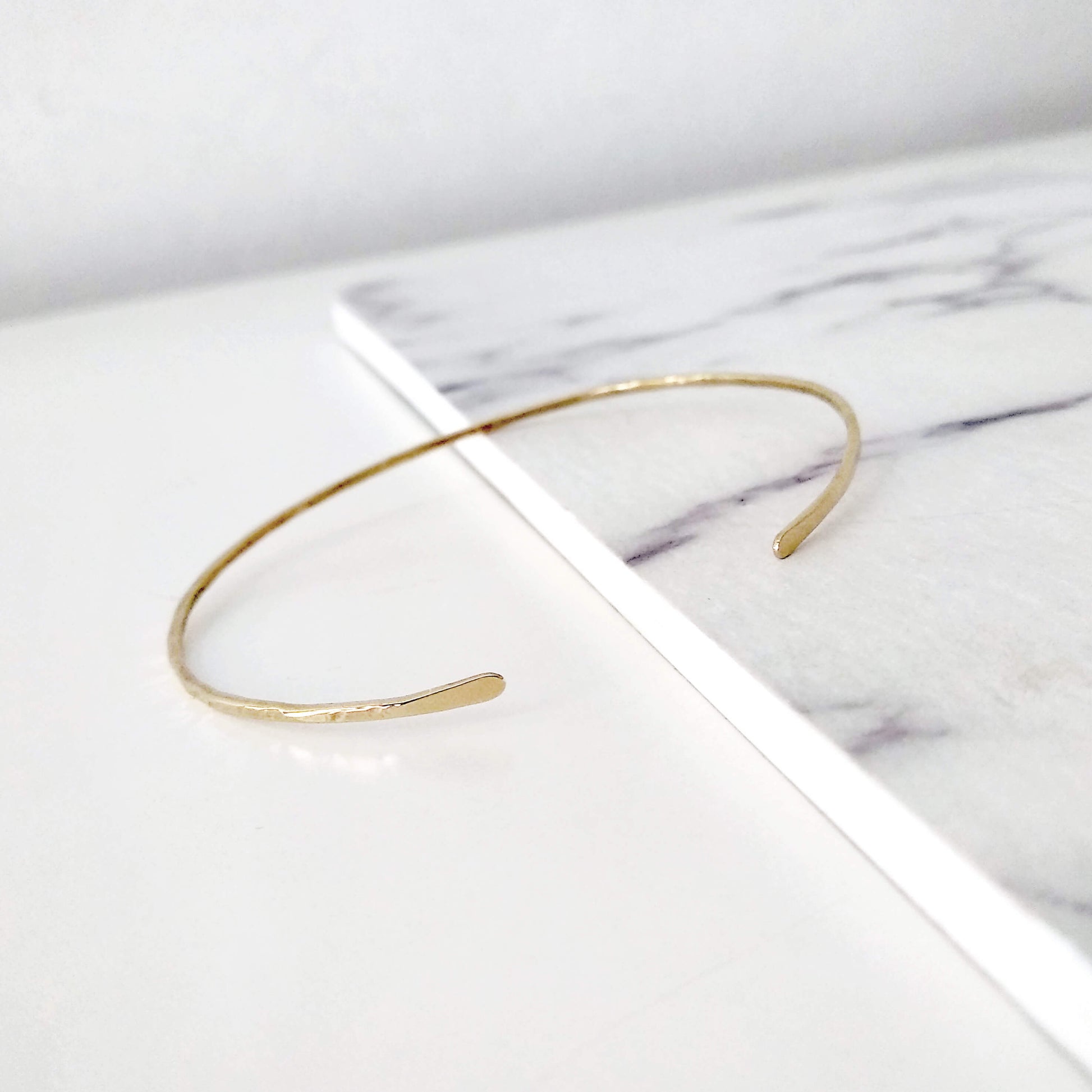 Thin gold hammered open bangle bracelet on a marble surface