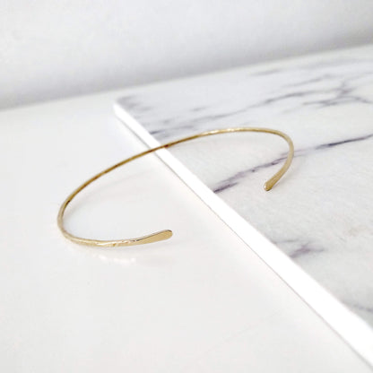 Thin gold hammered open bangle bracelet on a marble surface
