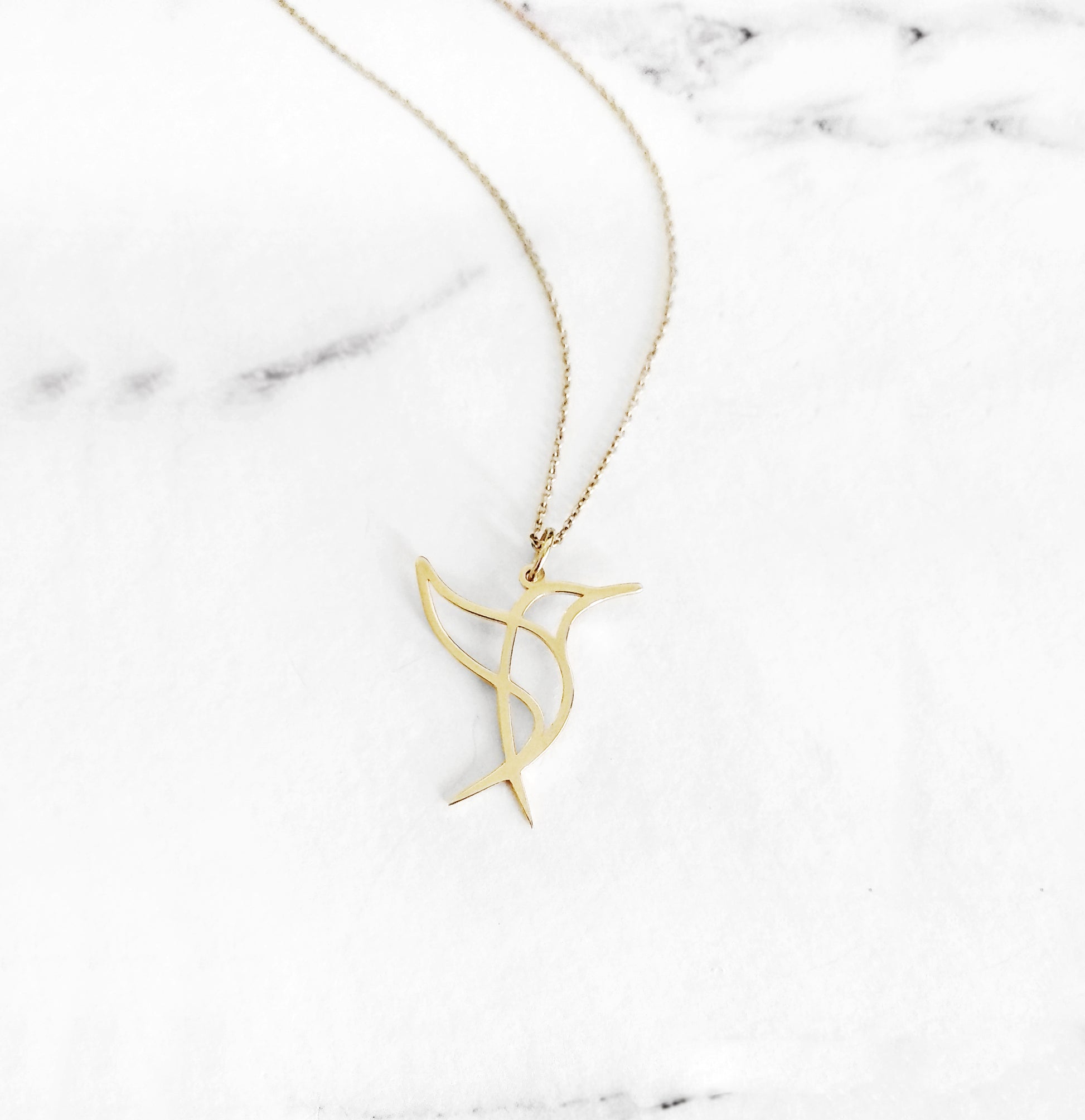 Close-up of a yellow gold necklace with a cutout origami style pendant in the shape of a hummingbird