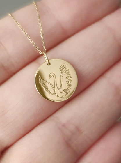 palm holding yellow gold necklace with a disc pendant engraved with a swan for size reference