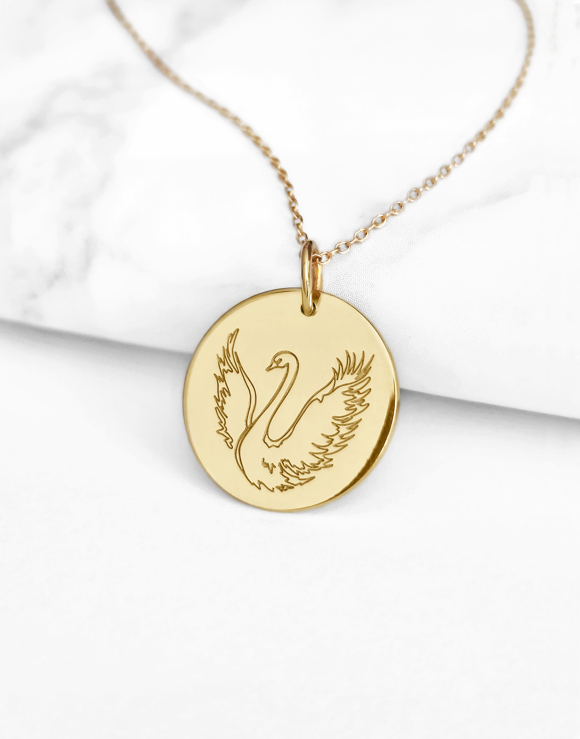 close up of yellow gold necklace with a 14mm disc pendant engraved with a swan with open wings