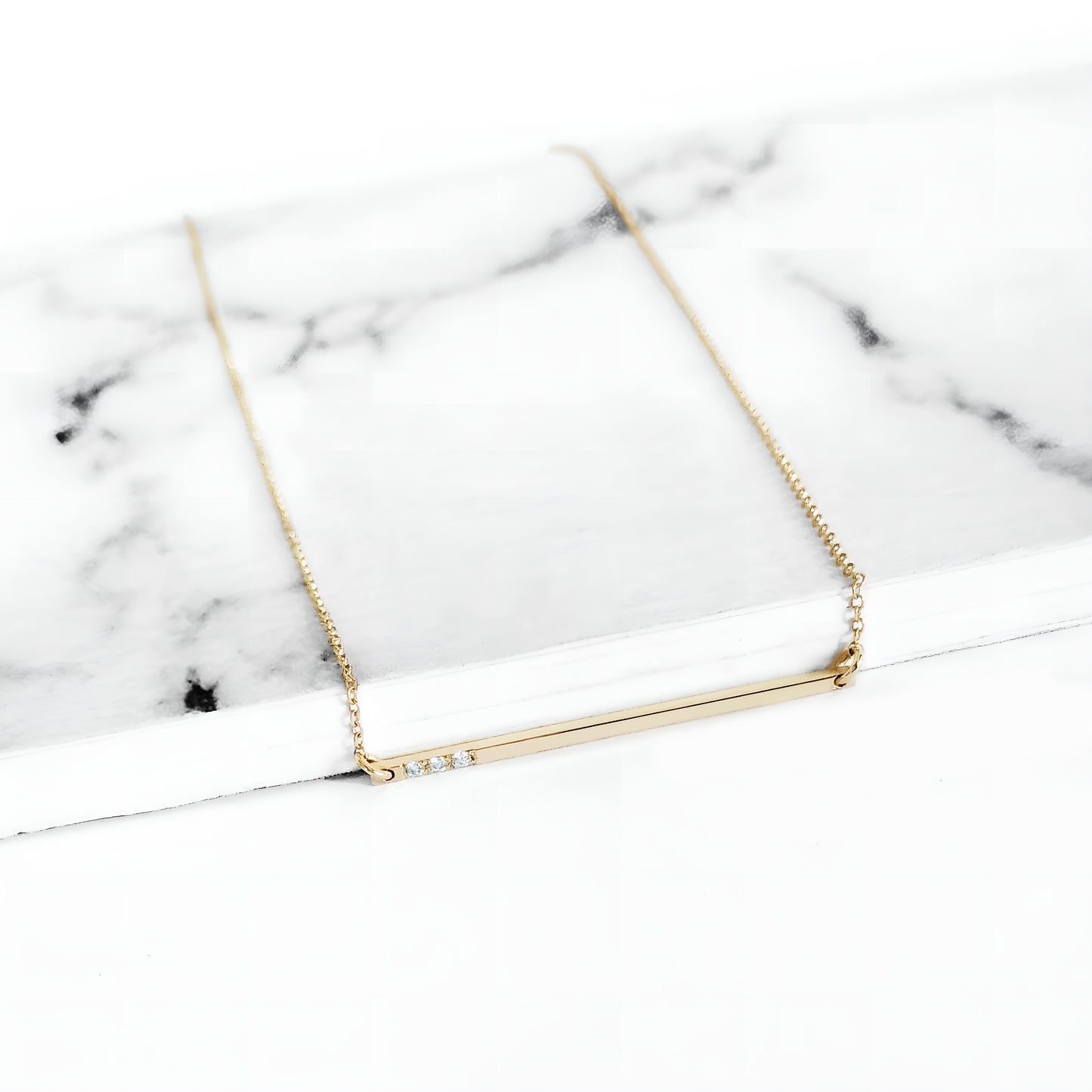 yellow gold thin bar necklace set with three tiny white diamonds