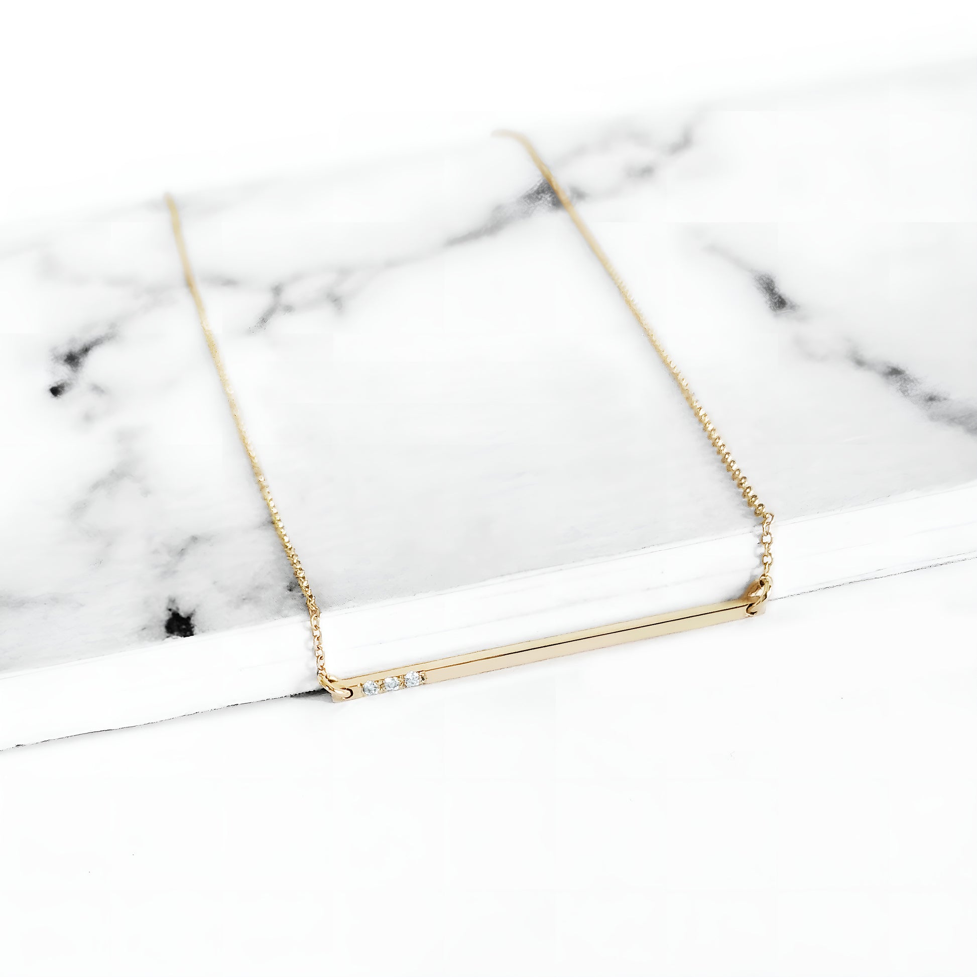 yellow gold thin bar necklace set with three tiny white diamonds